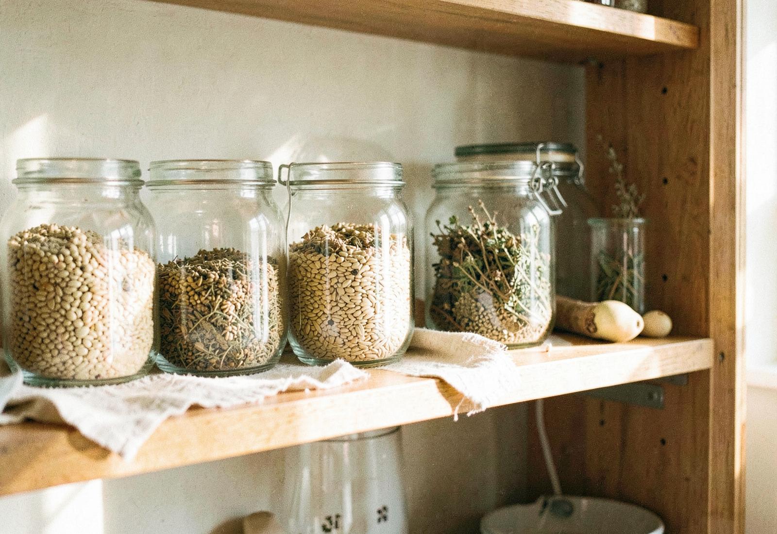 Glass jars of grains and dried herbs on a wooden pantry shelf in warm morning light